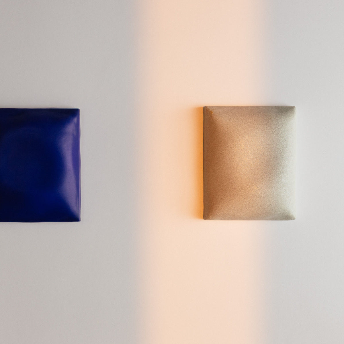 Two rectangular wall sculptures, one blue and one light beige, on a light grey background