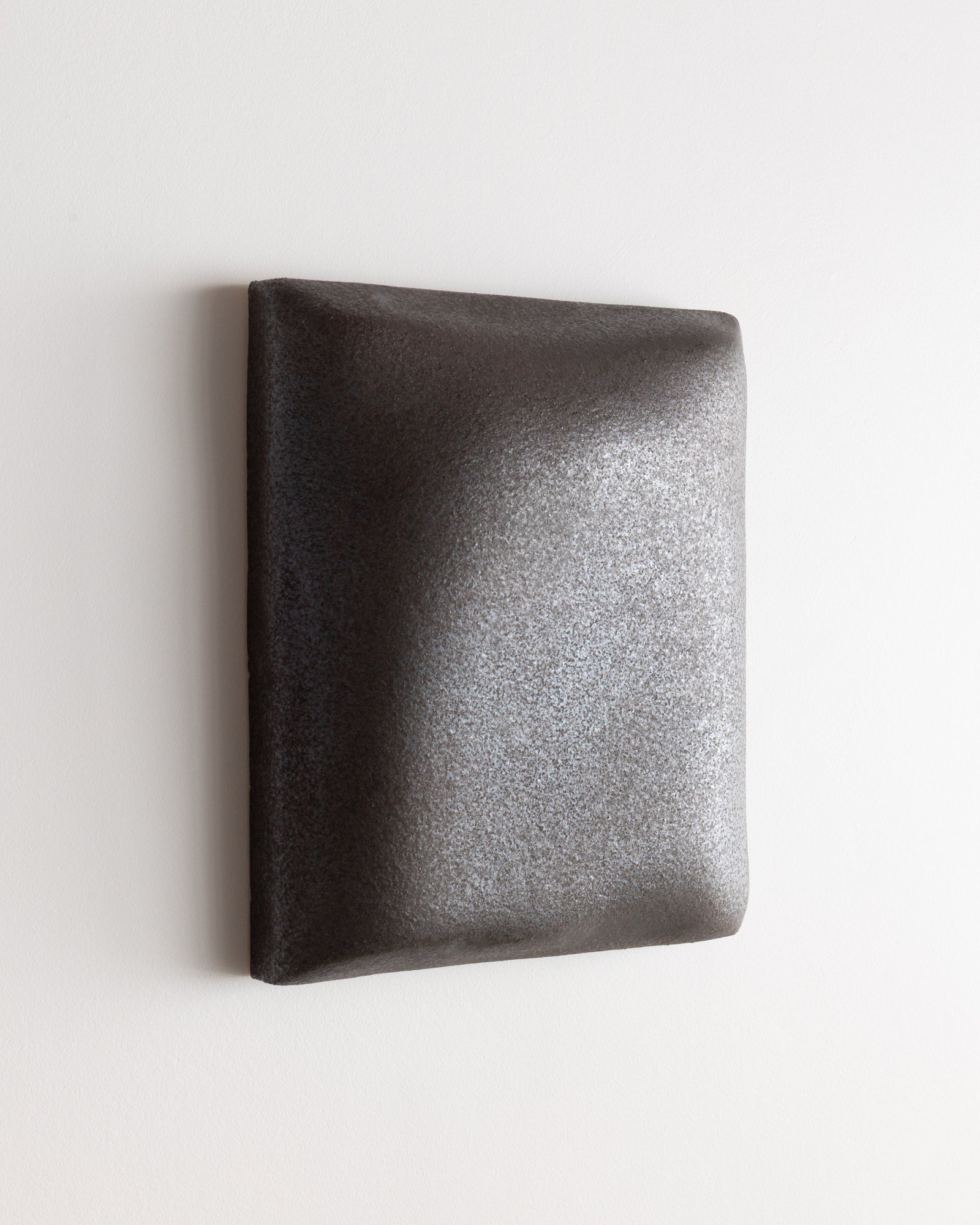 Angled view of a dark stone ceramic wall relief with softly rounded edges