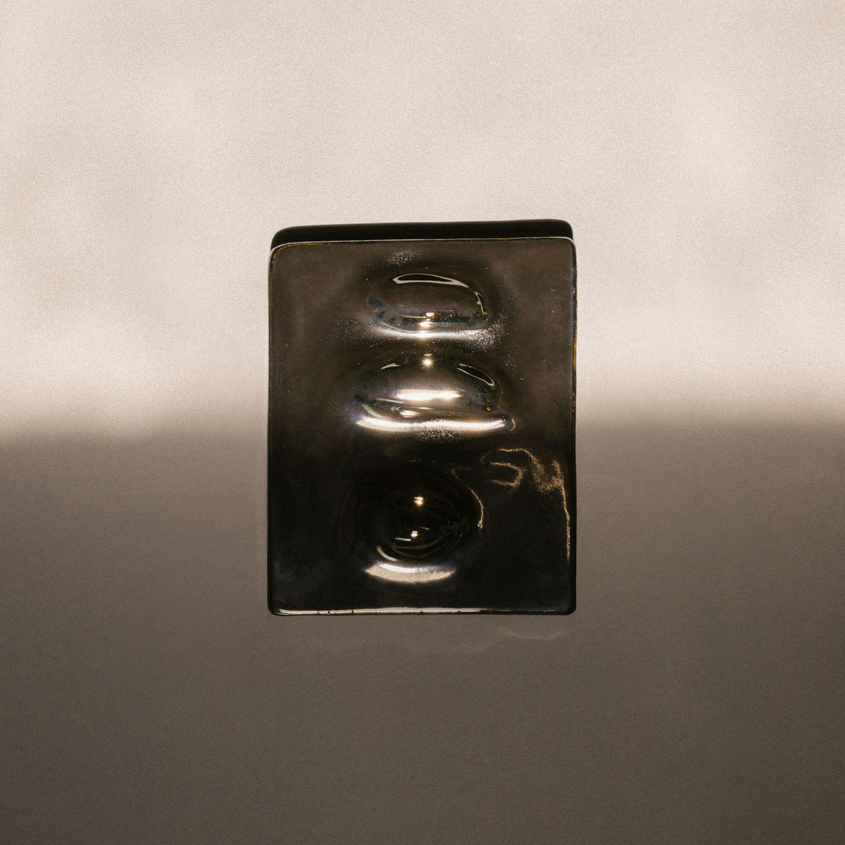 Small glossy black ceramic wall relief mounted on a neutral wall