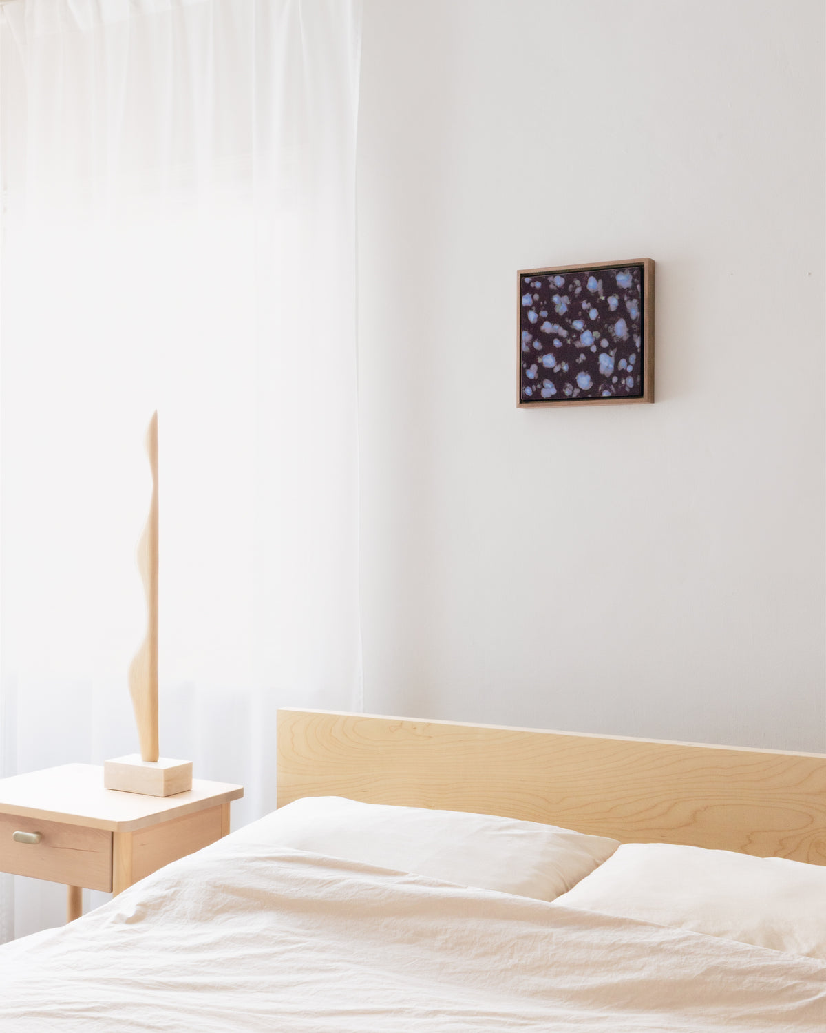 In-room view of "Snow on Petals" hanging above a bed in a quiet bedroom setting