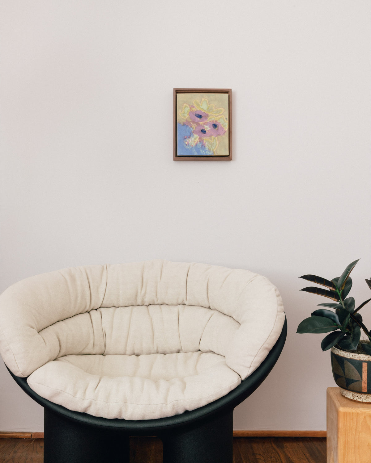 In-room view of "Breakfast Table" hanging above a cushioned chair beside a potted plant