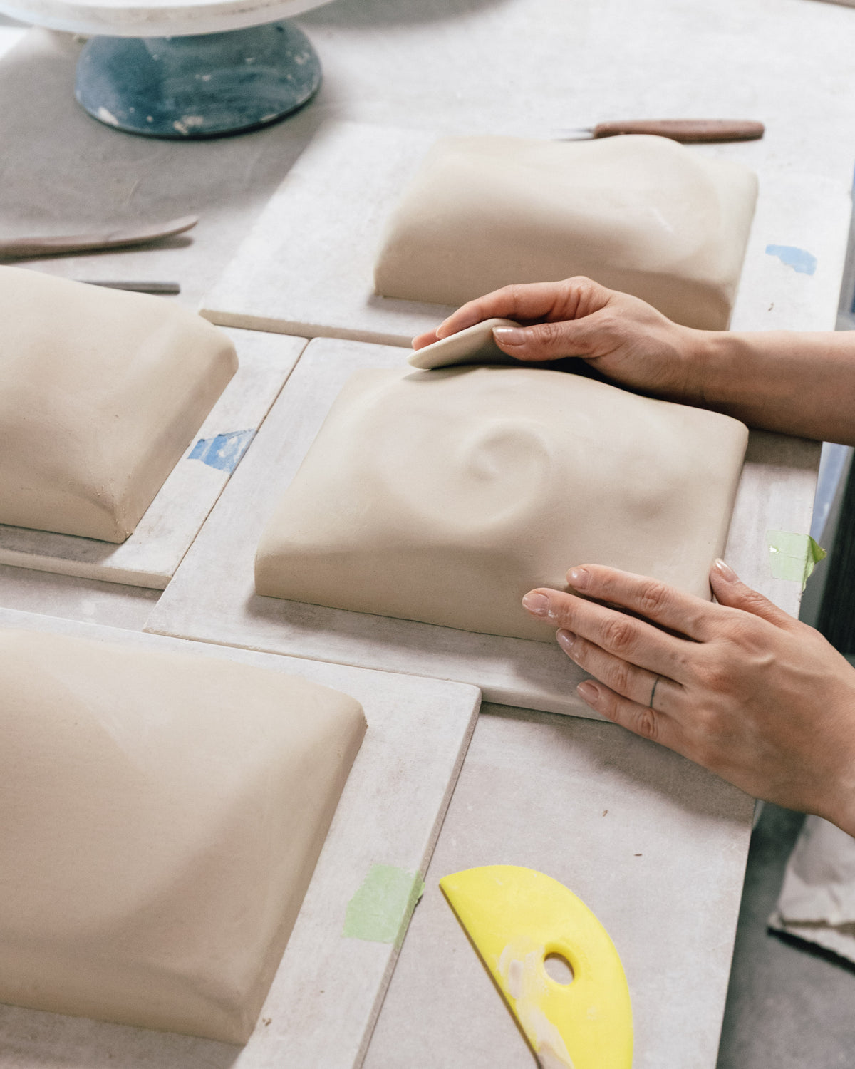 Hands shaping white ceramic relief tiles on a worktable