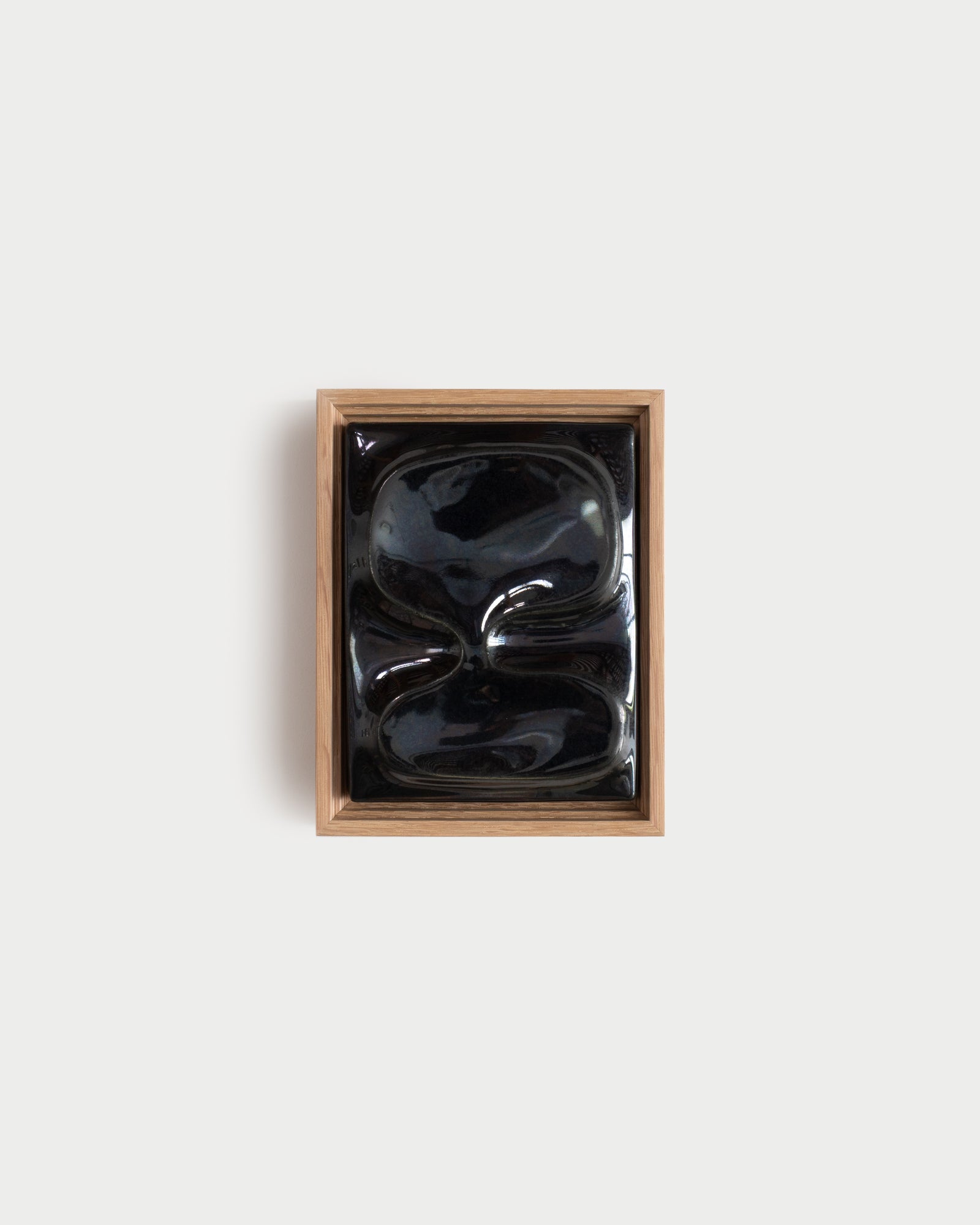 Small black reflective ceramic wall relief in a wooden frame