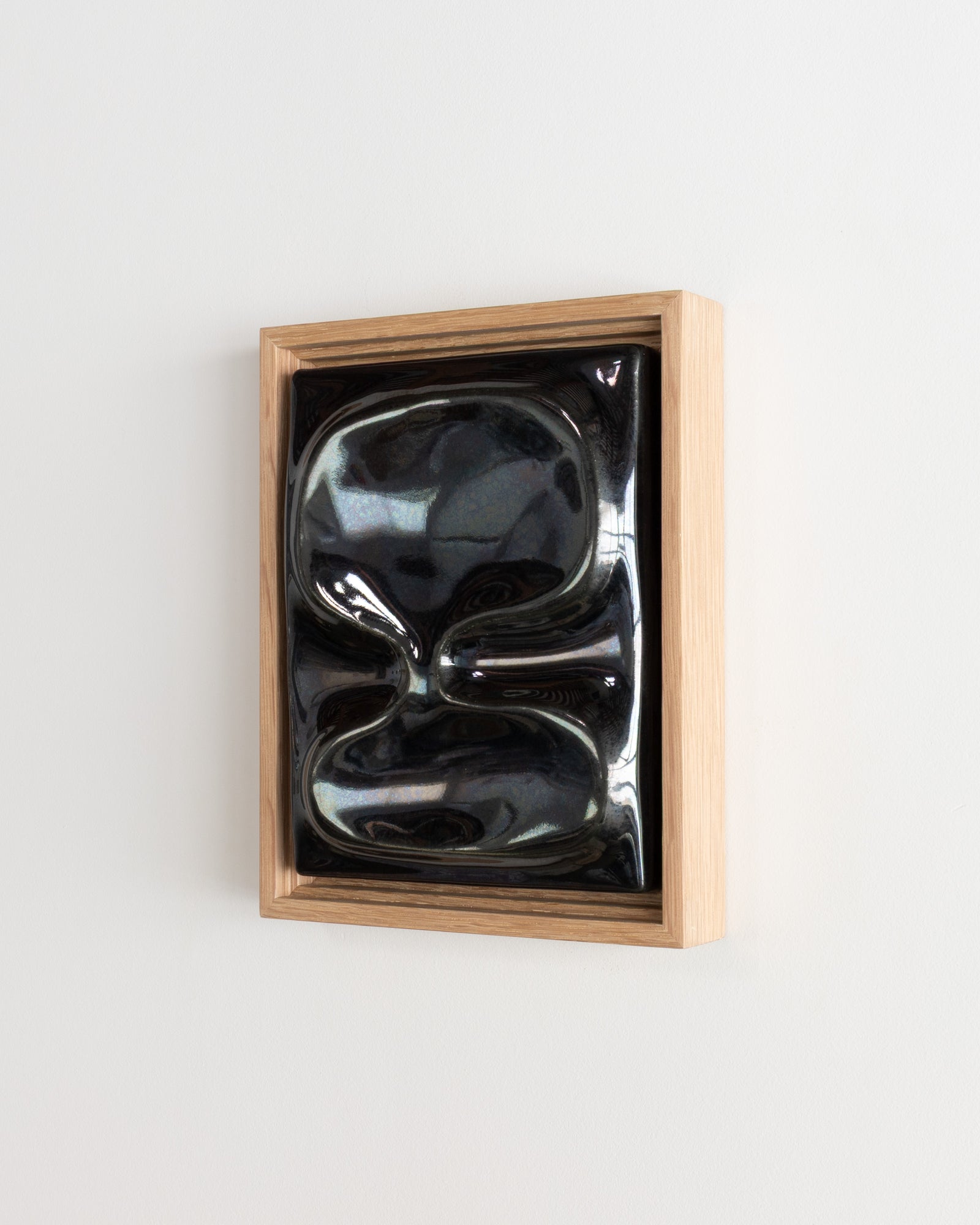 Small black reflective ceramic wall relief in a wooden frame on a white wall
