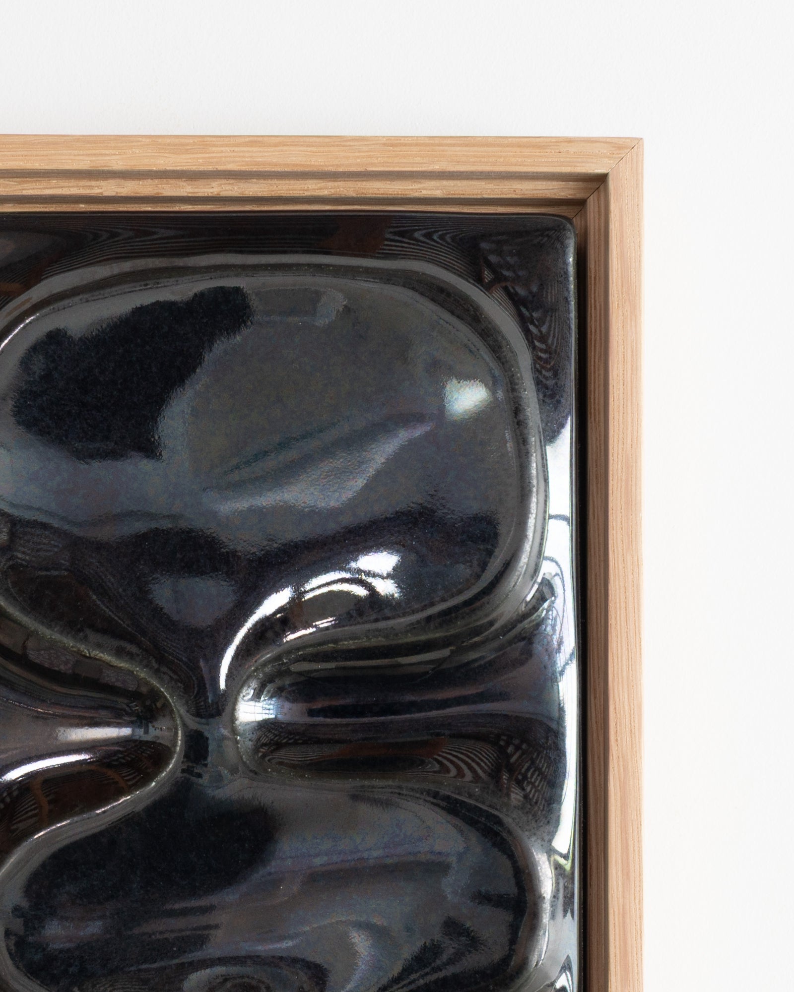 Close-up of glossy black ceramic relief forms in a wooden frame