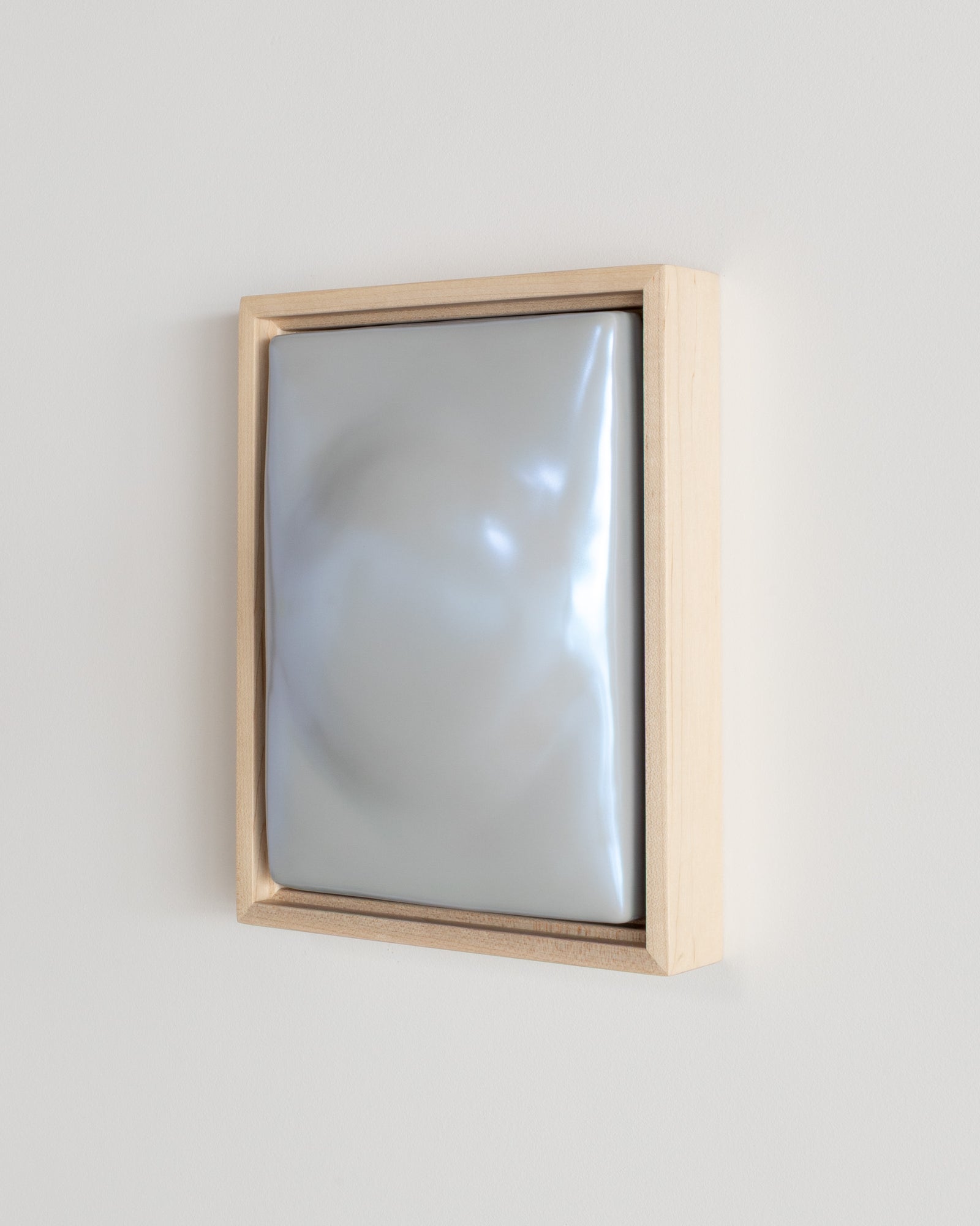 Angled view of a pale blue framed ceramic wall relief on a white wall