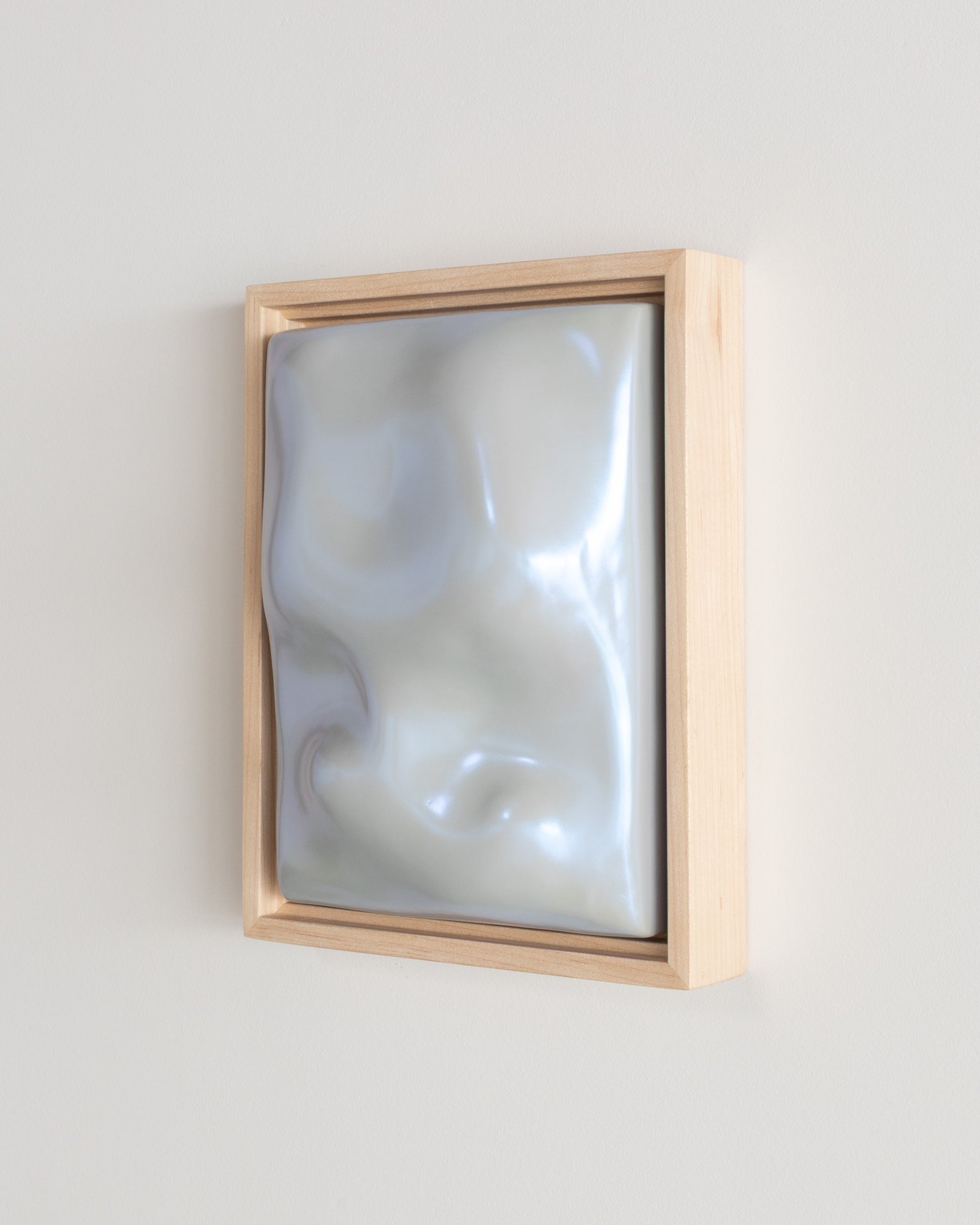 Angled view of a pale blue framed ceramic wall relief on a white wall