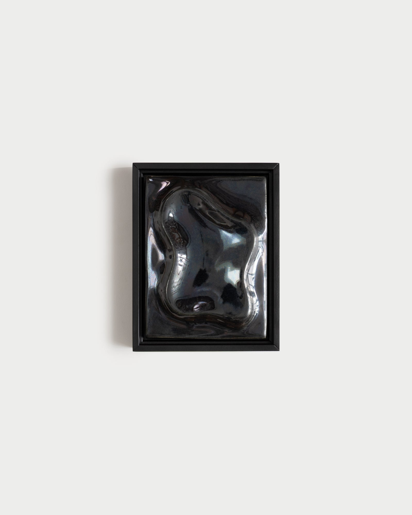 Black framed reflective ceramic wall relief on a white wall