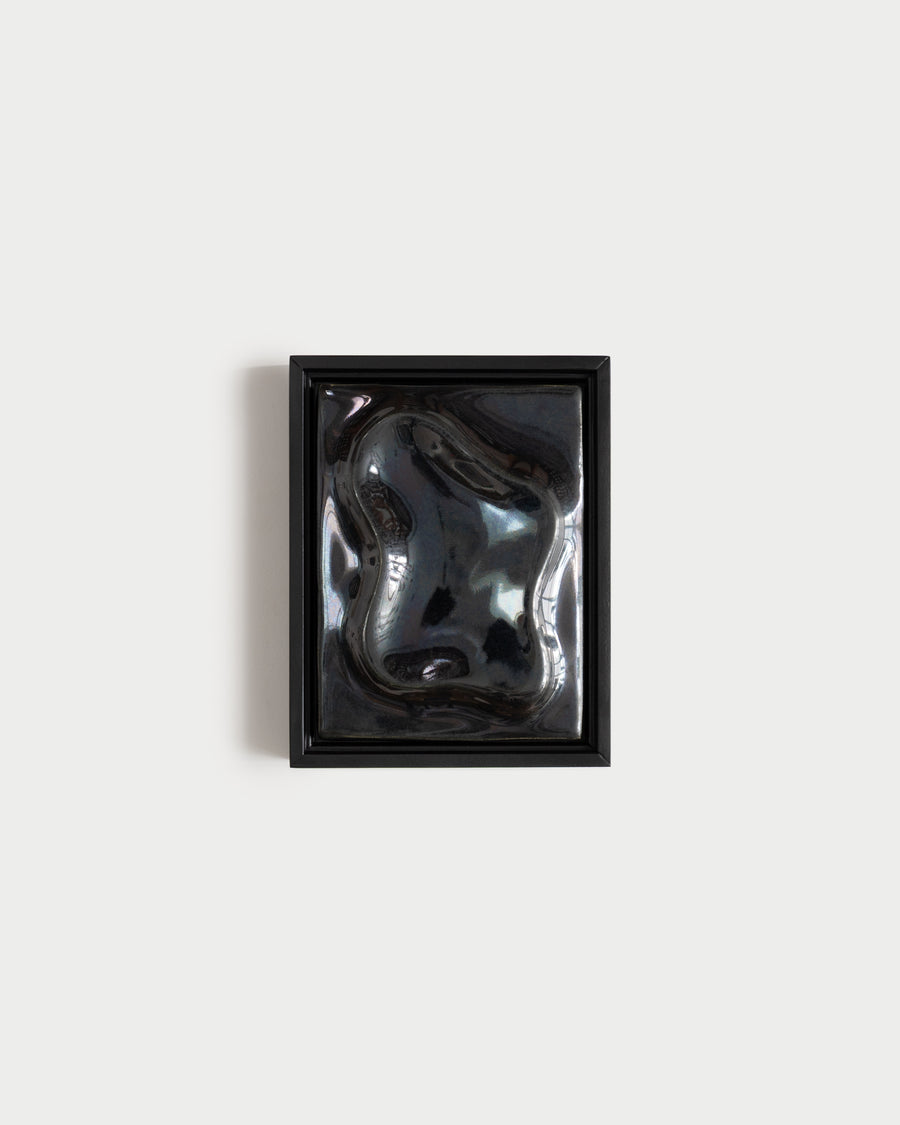 Black framed reflective ceramic wall relief on a white wall