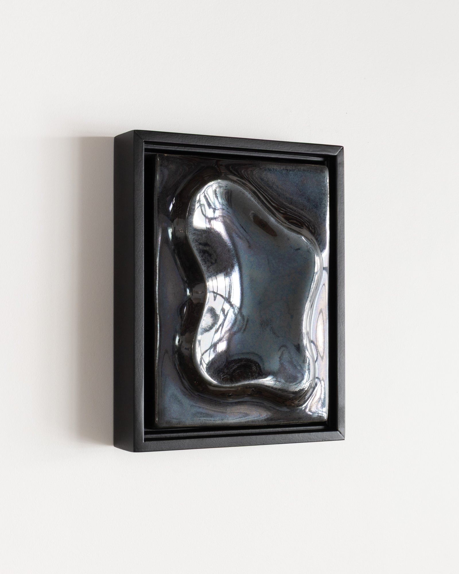 Angled view of a black framed reflective ceramic wall relief