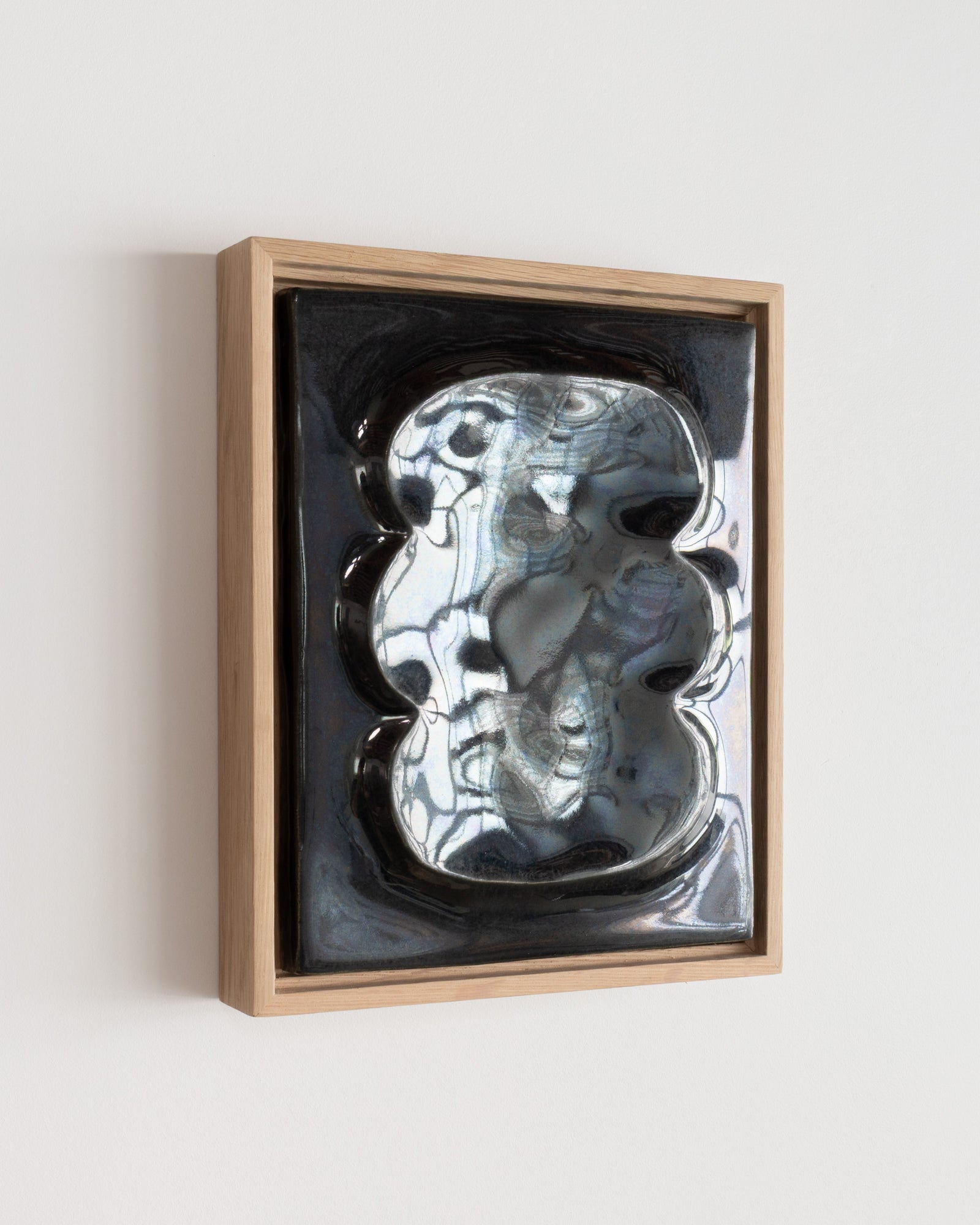 Angled view of a black framed ceramic wall relief with pale reflections