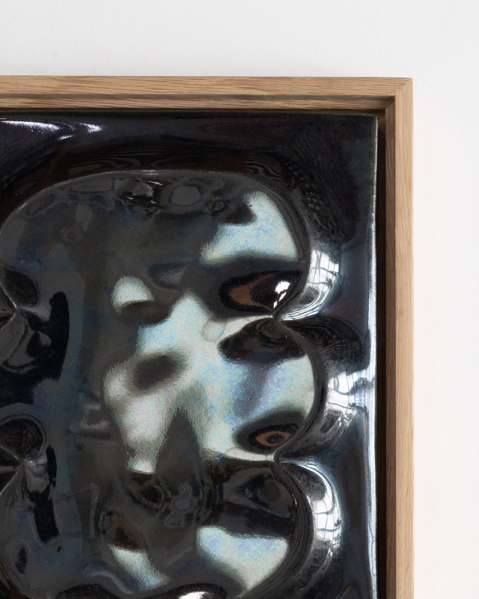 Close-up of black glossy ceramic raised forms in a wooden frame