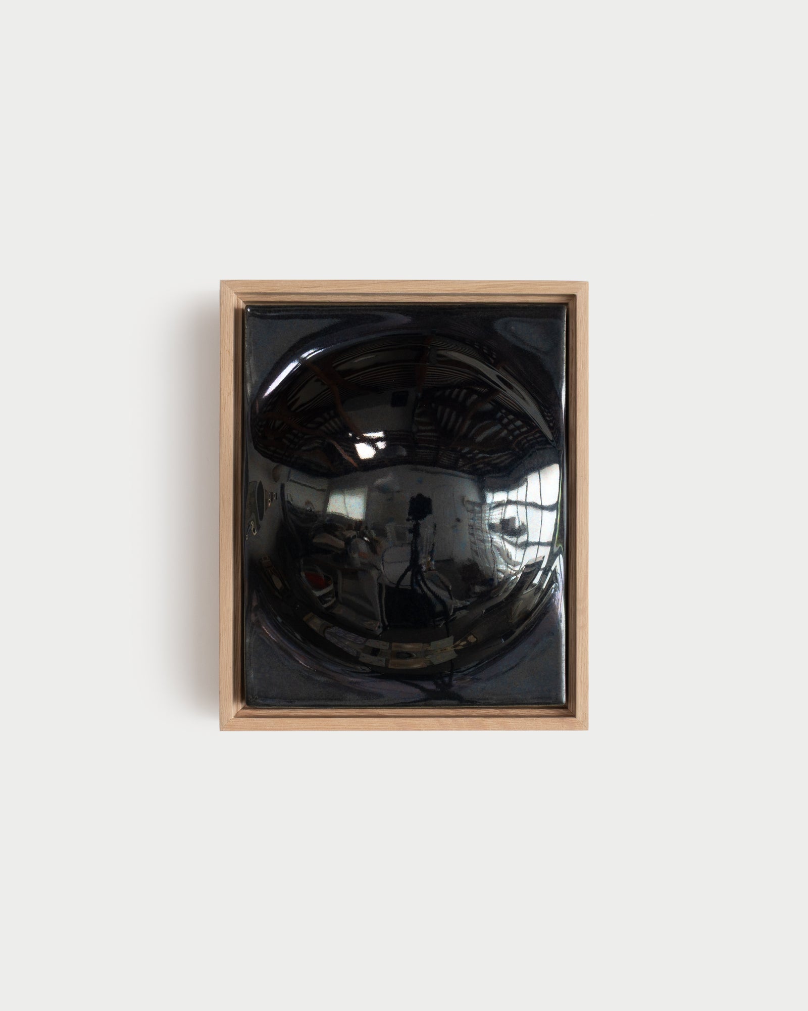 Small black framed ceramic wall relief with a large rounded form
