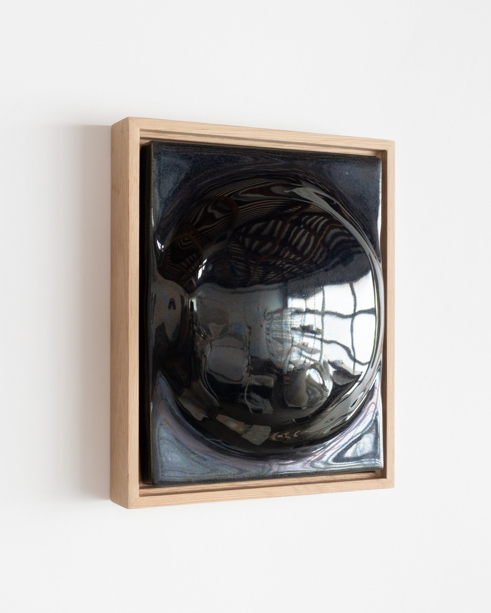 Angled view of a black framed ceramic wall relief with a glossy rounded form