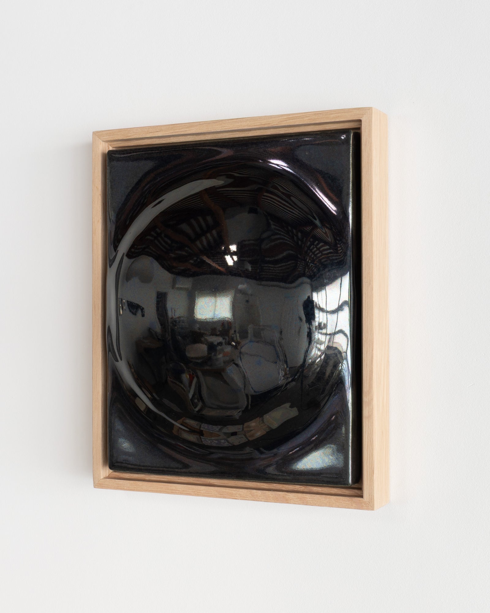 Angled view of a black framed ceramic wall relief with a large rounded form