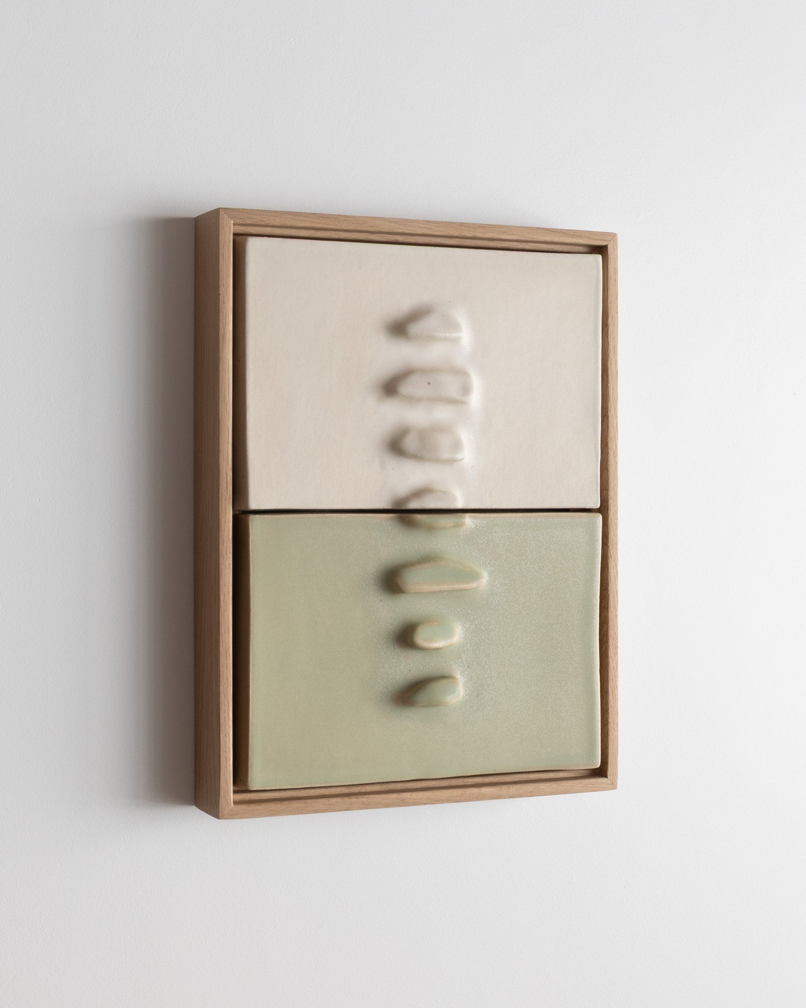 Angled view of a framed two-panel ceramic wall relief in white and pale green