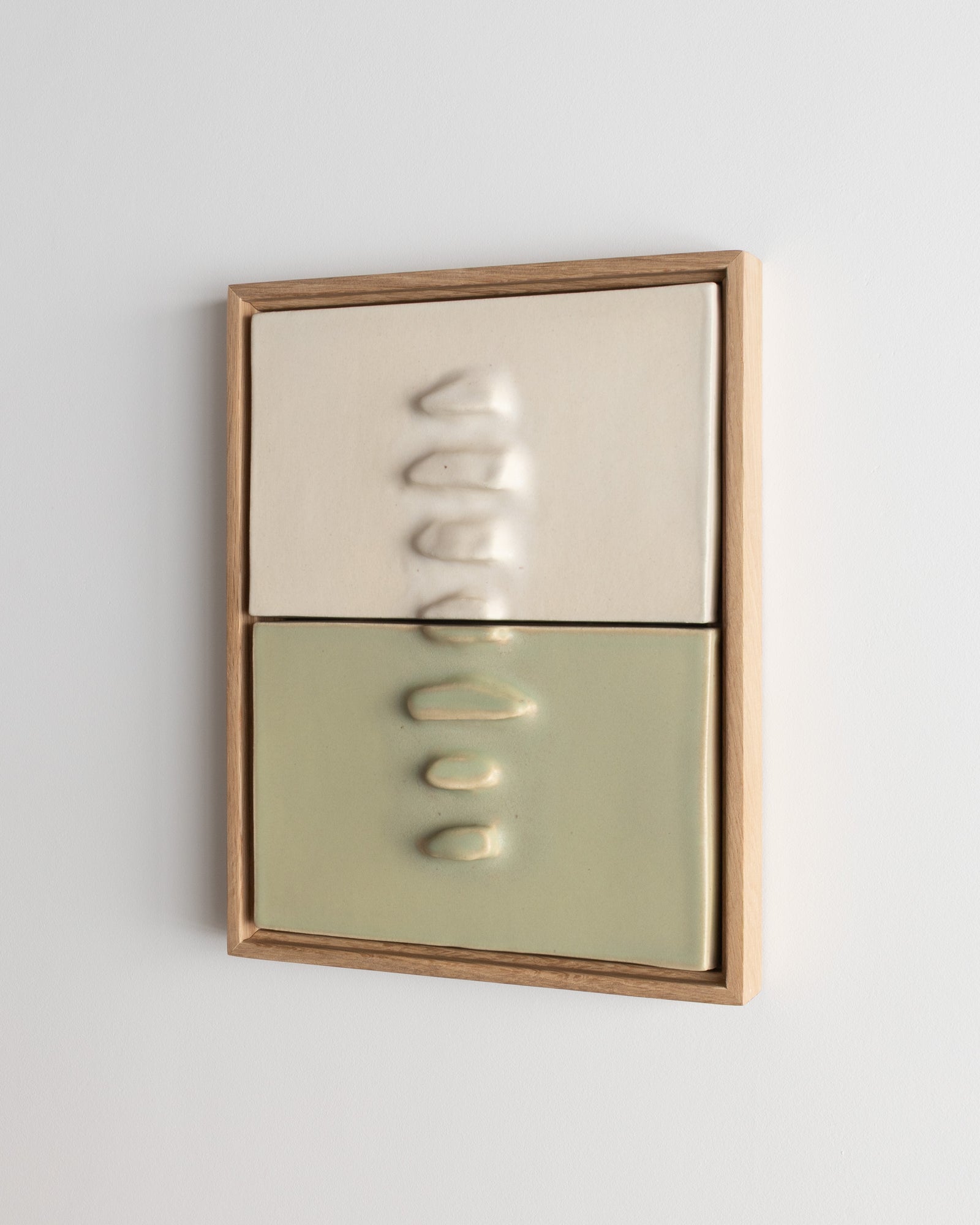 Framed two-panel ceramic wall relief in white and pale green on a white wall