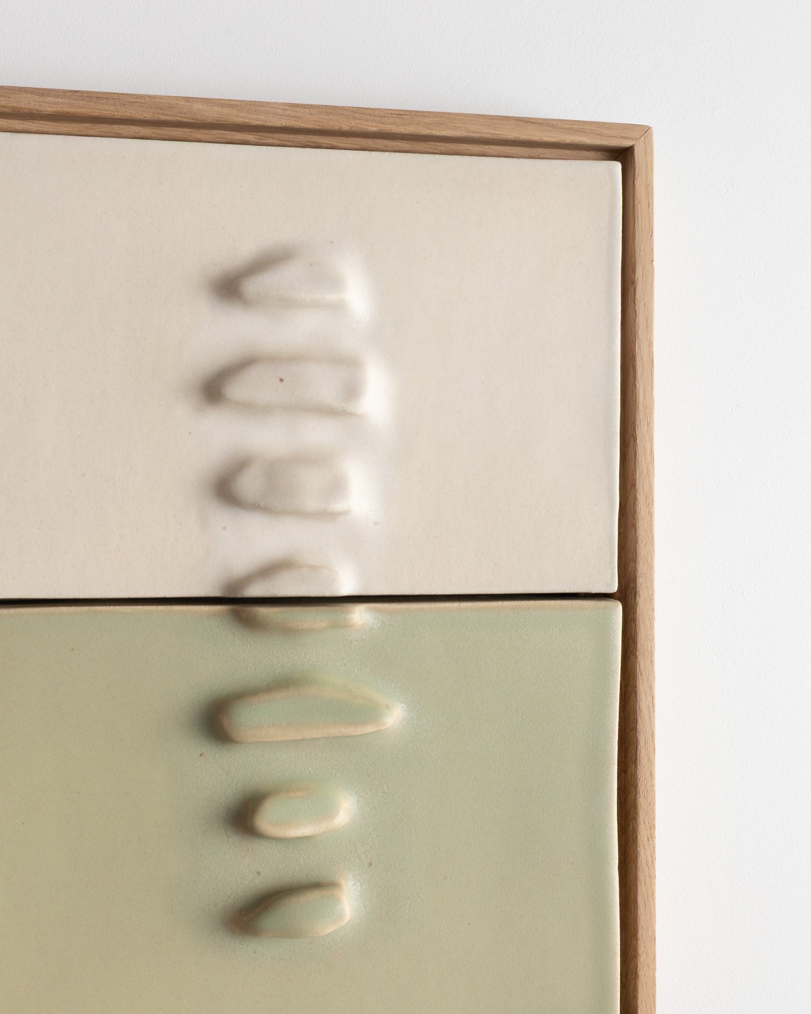 Close-up of a framed two-panel ceramic relief with white raised forms and pale green lower panel