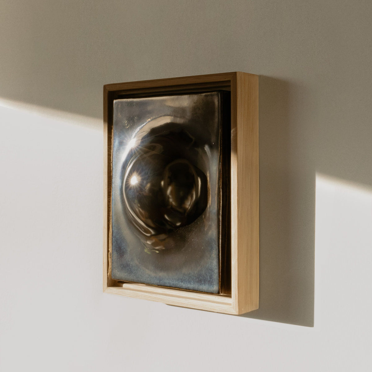 Framed metallic ceramic wall relief with a wooden frame on a neutral wall