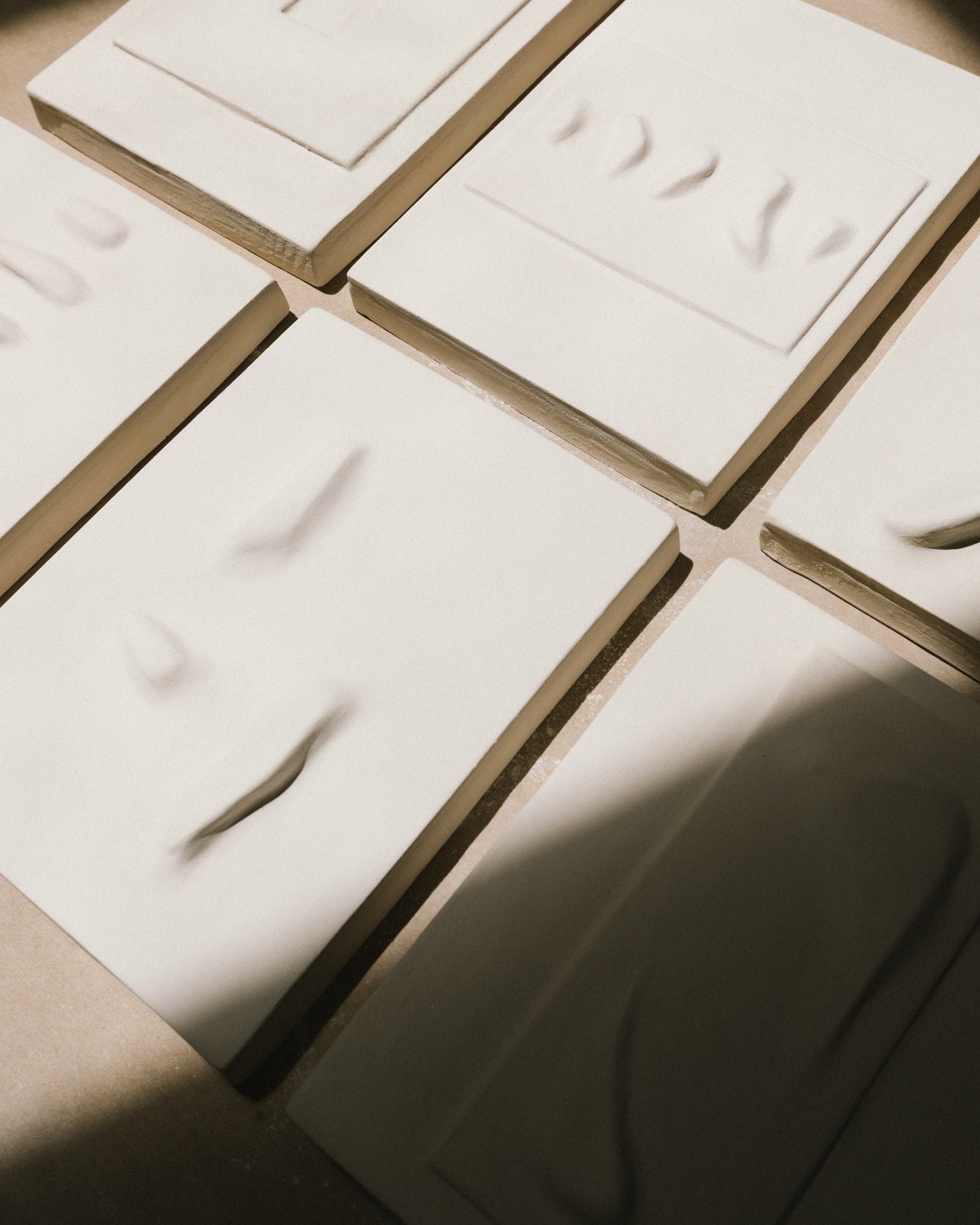 White ceramic relief tiles in progress on a tabletop